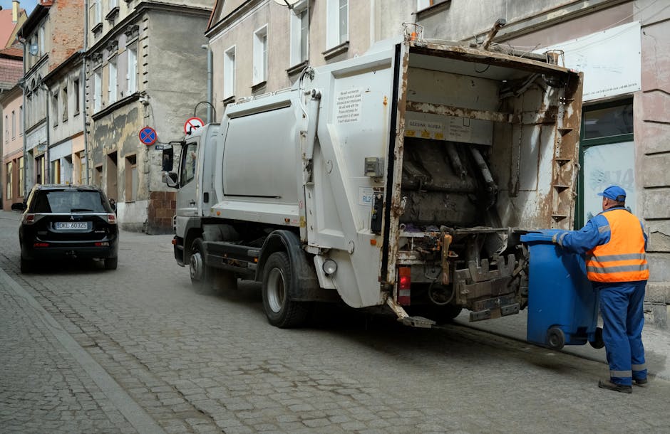 An outdoor urban scene depicts a large pile of rubbish overflowing from multiple waste bins placed on a paved sidewalk near a parking area. The waste includes a variety of materials such as crumpled c